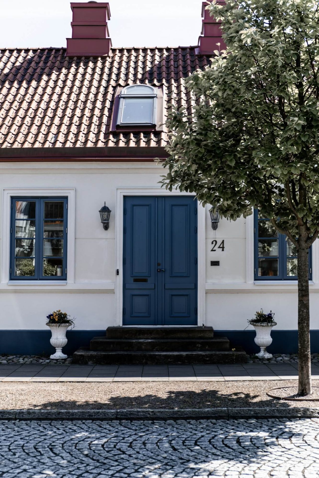 Med sin vita puts, blåa detaljer runt dörr och fönster, samt kullerstensbelagda trottoaren, framstår huset som en klassisk skönhet