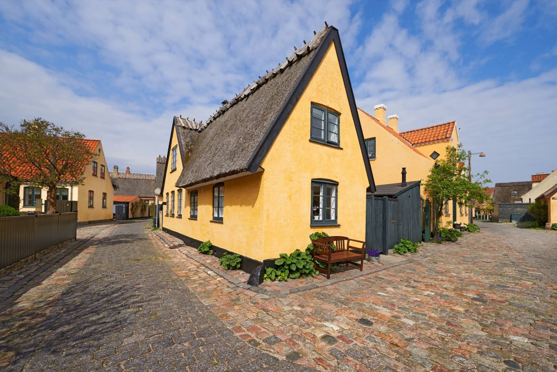 På en bedårande gata finner man ett hus med en renoverad, guldfärgad fasad i gammal stil, svarta fönsterdetaljer och ett tak täckt av halm